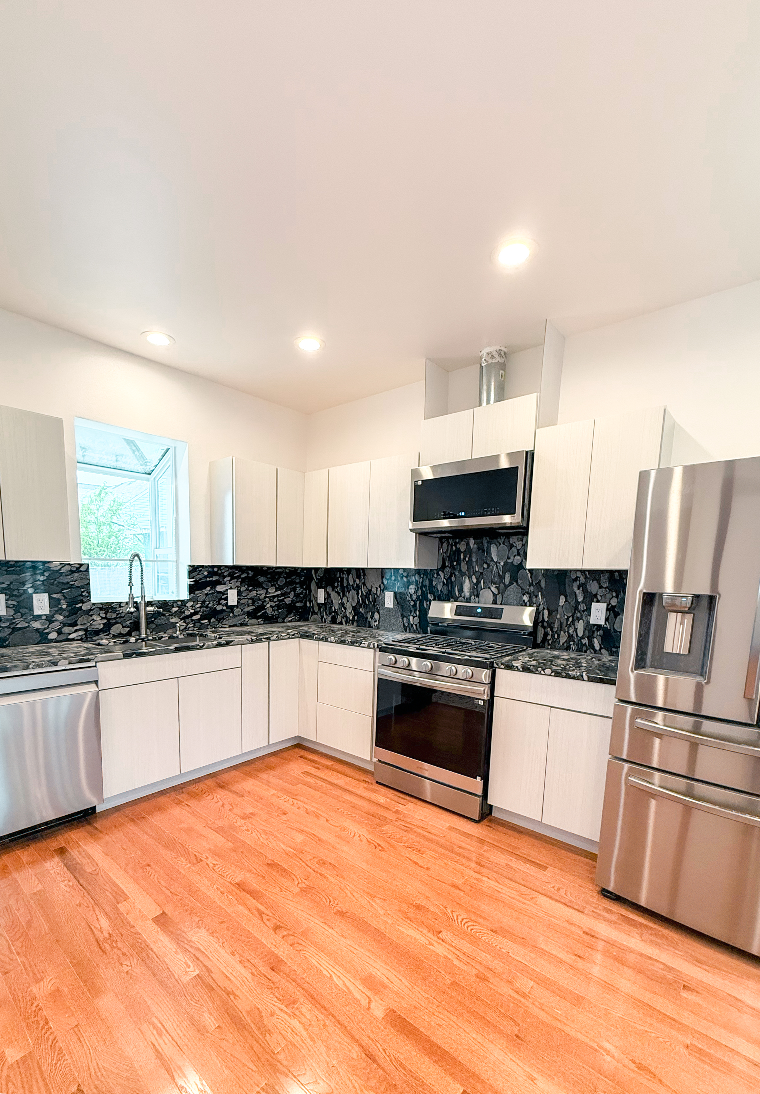Kitchen with stone backsplash, stainless appliances, and hardwood floors.